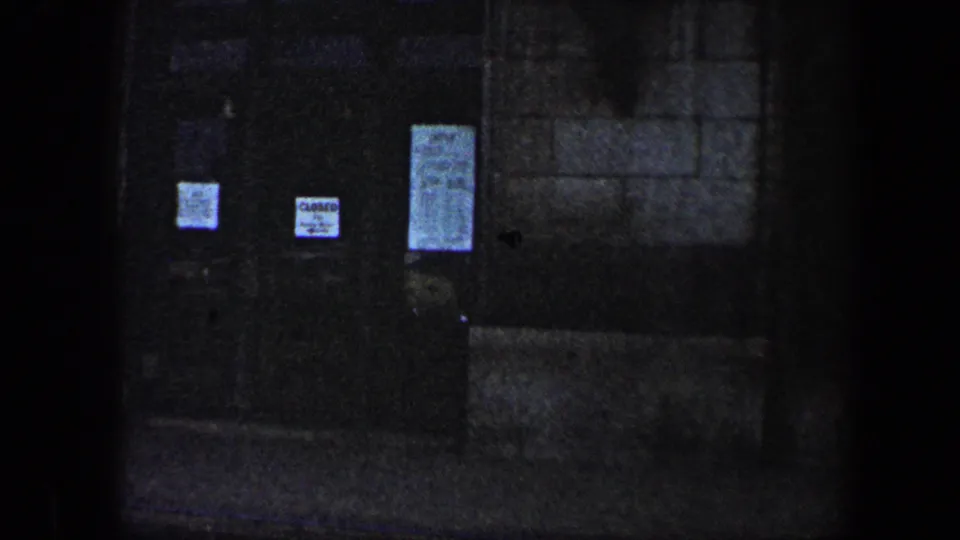 Dim 1960 Baltimore exterior view of a dark doorway with several paper notices posted on the doors.