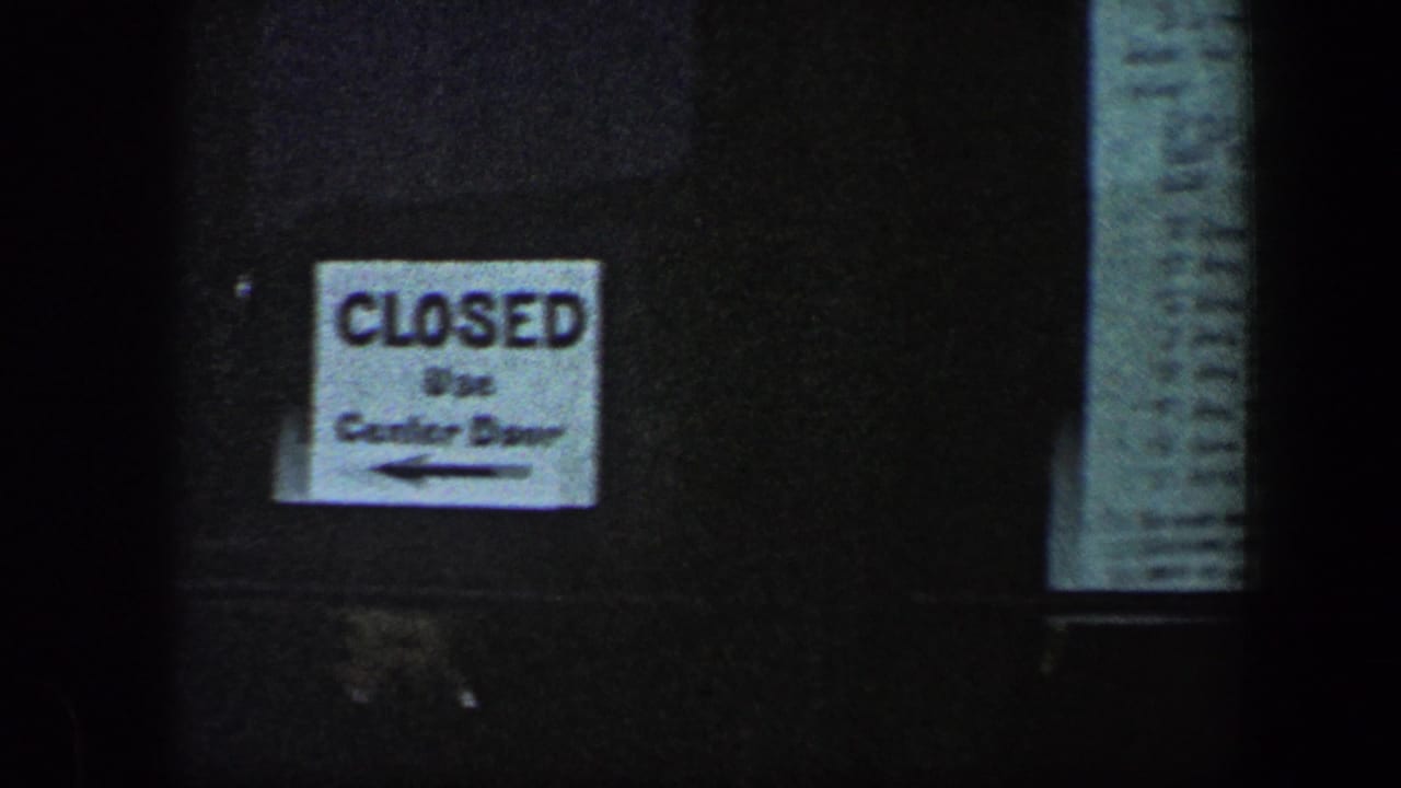 Closed sign with an arrow beside a narrow posted paper on a dark exterior surface.