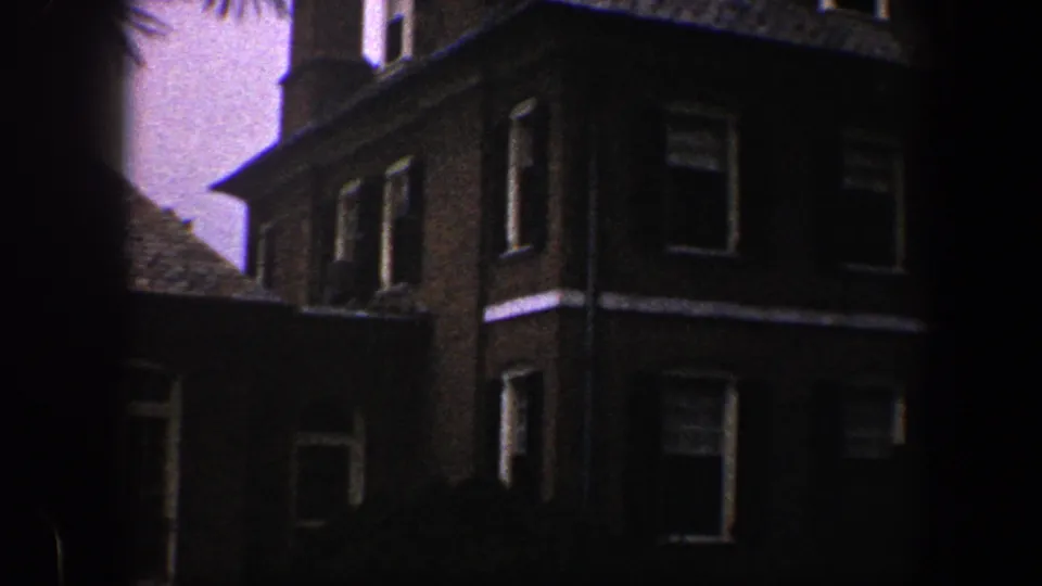 Corner of a brick house with white trim and dark windows, shown in a short 1960 Baltimore exterior sequence.