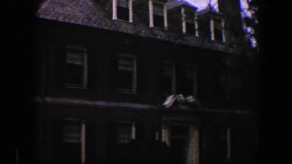 1960 Baltimore home-movie frame of a dark brick residence with dormer windows, front windows, and a partially visible columned entrance.