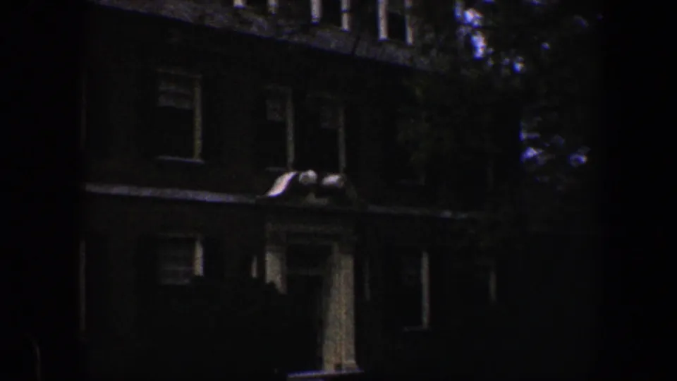 1960 Baltimore frame showing a darker, closer view of the brick house front, including windows, columns, and trees at the edge of the facade.