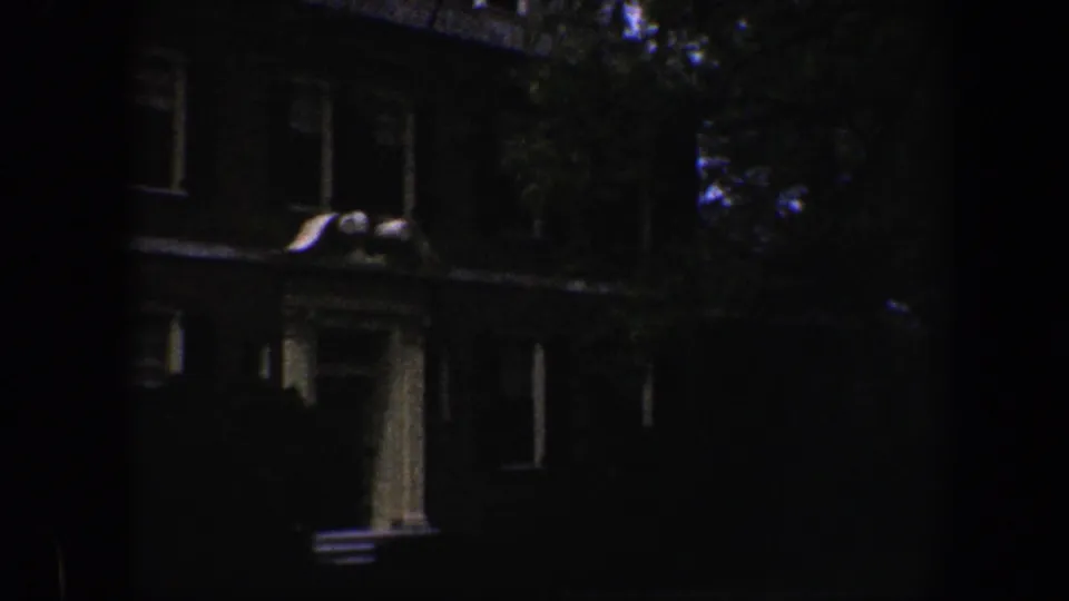 1960 Baltimore 8mm frame with a columned entrance, brick facade, windows, tree foliage, and strong shadow across the house front.