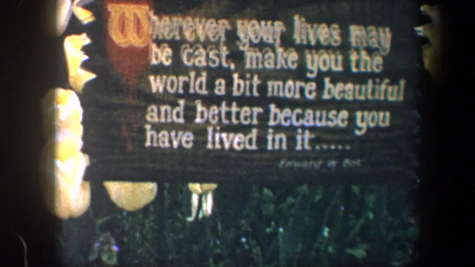 Final 8mm frame of the Baltimore garden sign, with the inspirational quote visible above roses, foliage, and small pale garden elements.