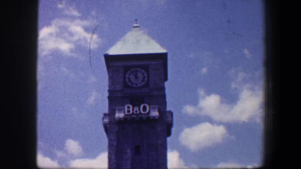 Clearer 1960 Baltimore home-movie frame of the B&O clock tower beneath a blue sky with scattered clouds.