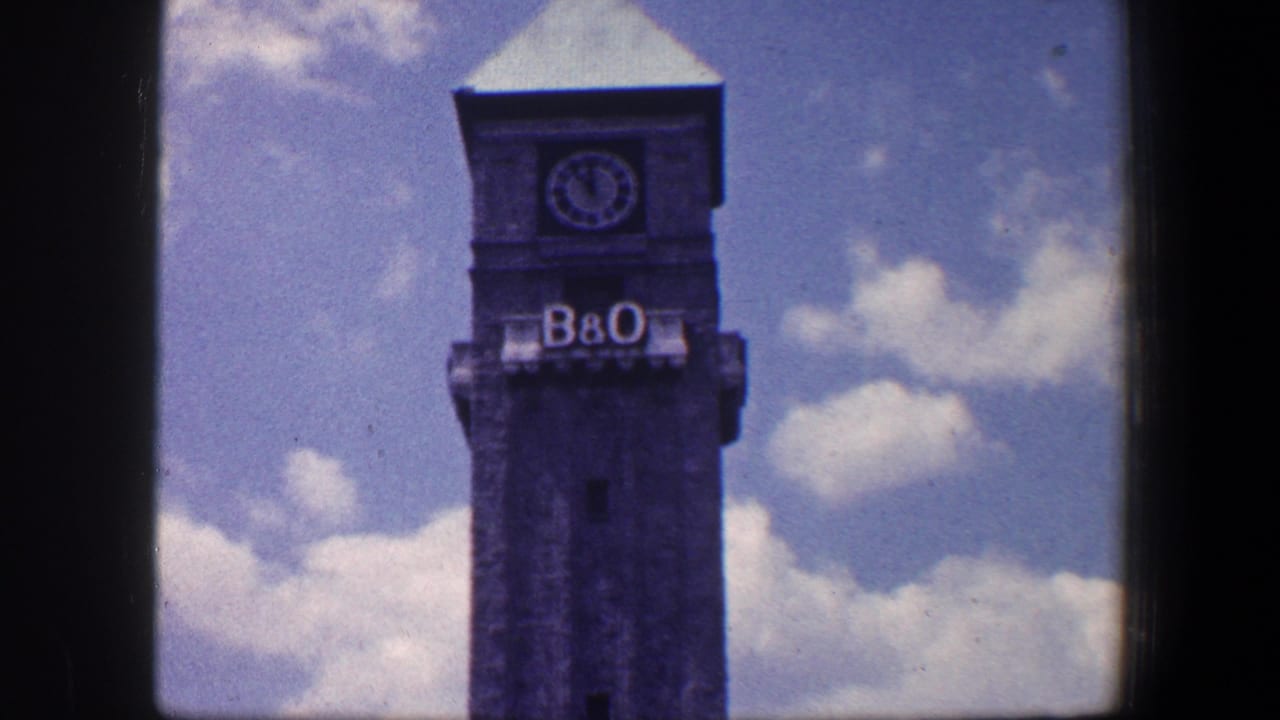 Upper B&O clock tower with clock face and lettering against clouds.