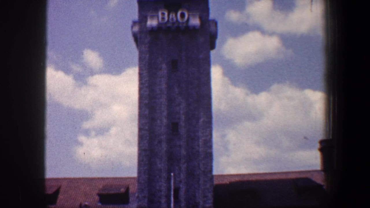 Stone tower with B&O letters above a red-roofed building under cloudy sky.