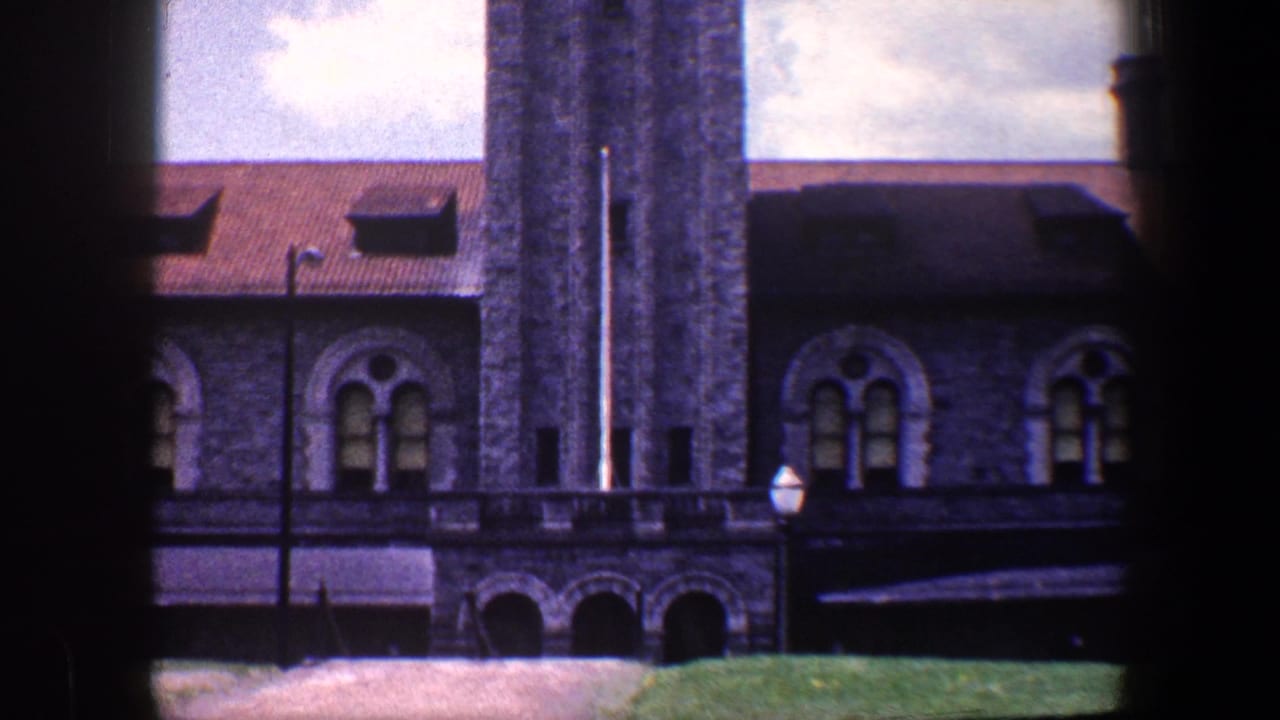 Stone building with tower, arched windows, red roof, and dark window frame in foreground.