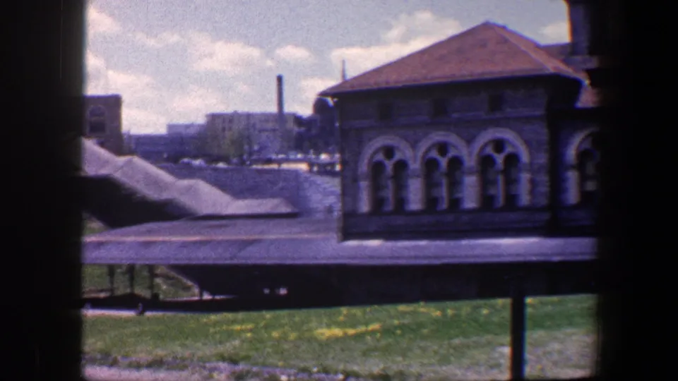1960 Baltimore exterior showing a stone building with arched windows, red roof, covered walkway, lawn, and distant urban structures.