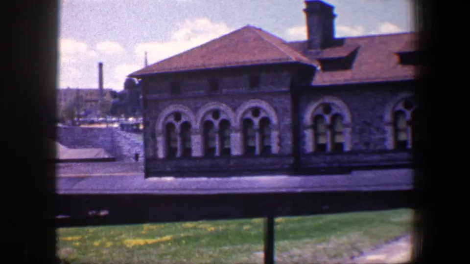 1960 Baltimore 8mm frame of a stone facade with arched windows, red roof, lawn, and dark foreground window framing.
