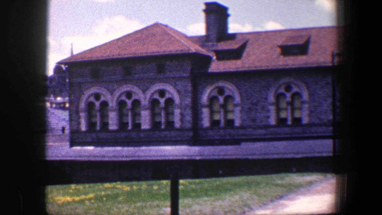 1960 Baltimore 8mm frame showing a stone building facade with arched windows, red roof, grassy foreground, and dark gate-like edges.