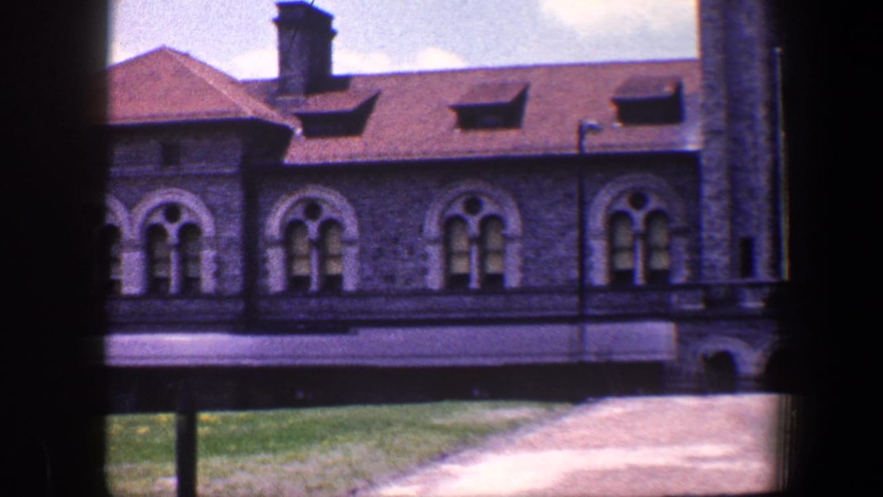 Stone building exterior with arched windows, red roof, path, grass, and dark vertical edge.