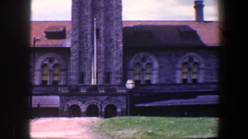 1960 Baltimore 8mm frame with the tower centered beside the stone facade, showing arched openings, red roof, grass, path, and lamp post.