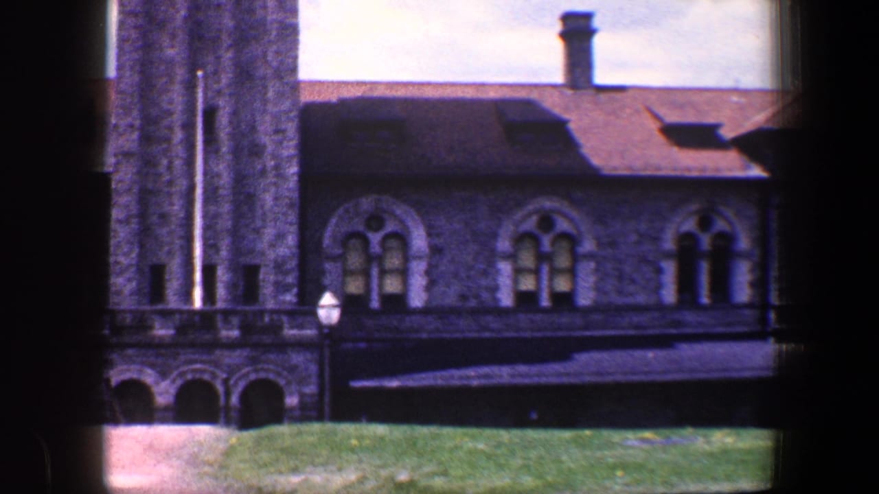 Stone building facade with arched windows, tower edge, lawn, and lamppost.