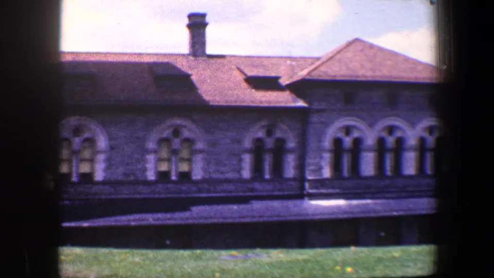 1960 Baltimore frame of the historic stone building with repeated arched windows, a pitched roof, roof vents, and lawn in front.