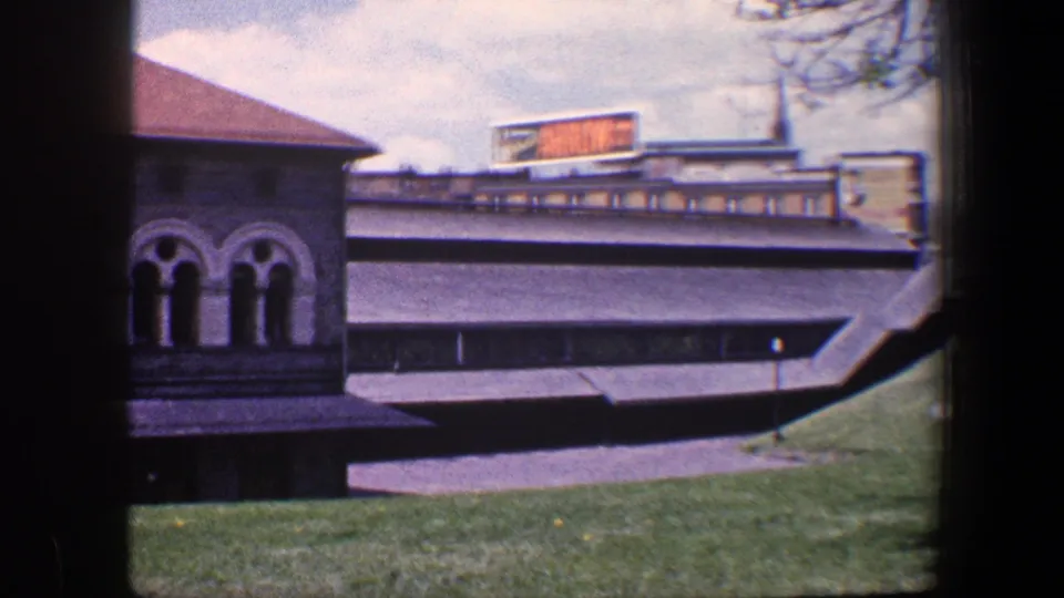 1960 Baltimore frame with arched stone windows at left, grass and walkway below, and an Arrow 77 sign on a nearby structure.