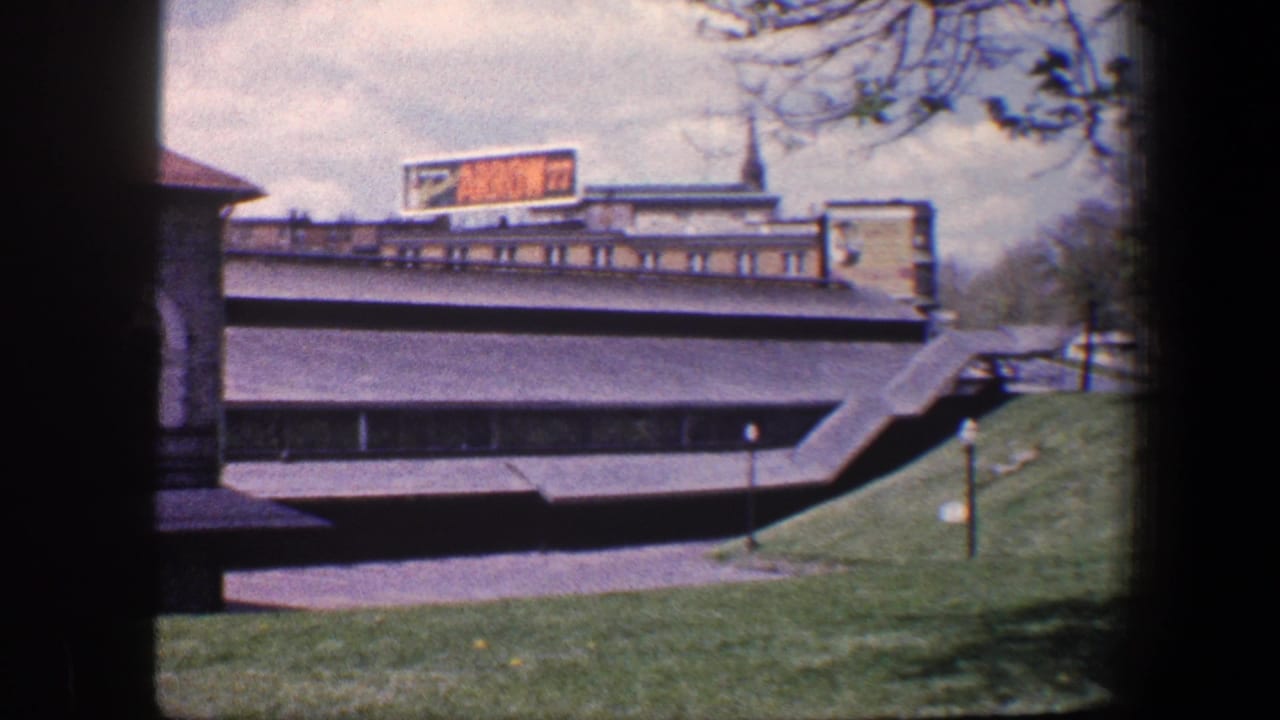 1960 Baltimore exterior showing grass, paved paths, steps, bare trees, and an ARROW 77 sign above a modern building.