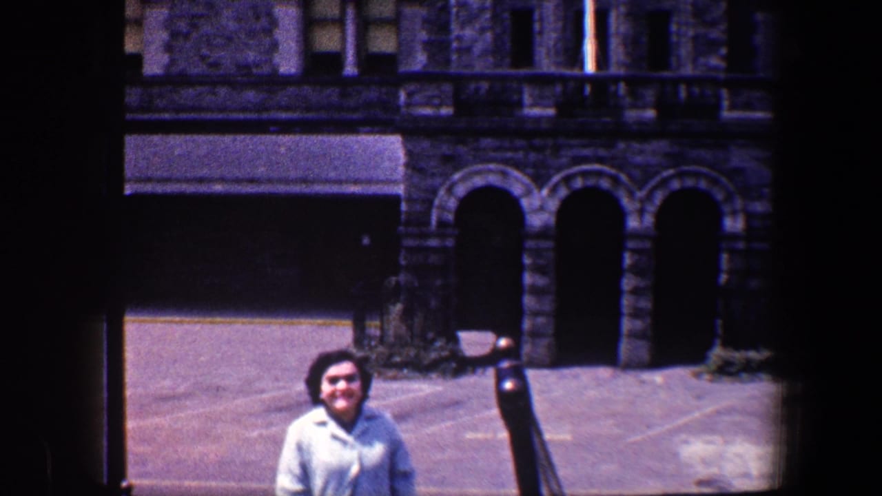 Woman in a pale suit stands outside a stone building with arched doorways.
