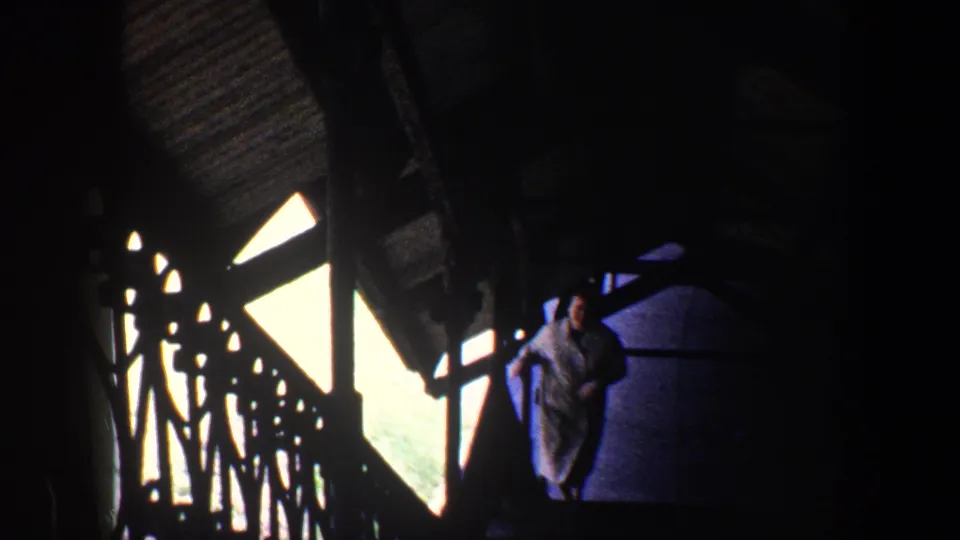 1960 Baltimore 8mm frame showing a woman in a grey coat climbing stairs beside ornate railings and bright exterior light.