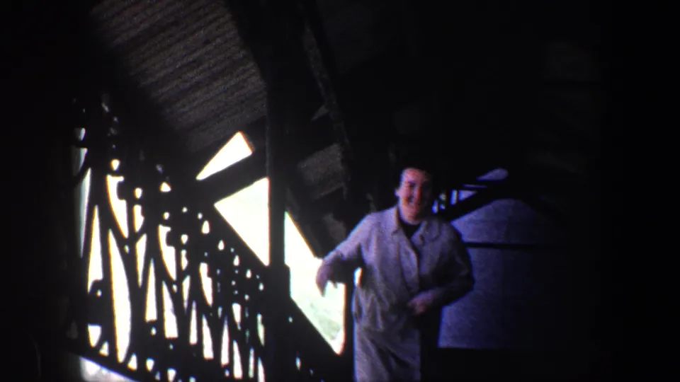 Near the end of the clip, the smiling woman is framed beside the railing in a dark Baltimore interior, with bright window shapes behind her.