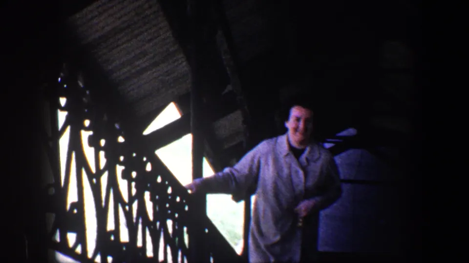 A woman in a light coat smiles beside decorative railings inside a shadowed Baltimore historic-site structure, circa 1960.