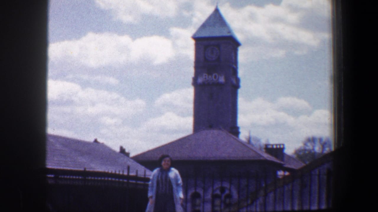 A woman poses outdoors near railings with the B&O clock tower and rooftops visible behind her in Baltimore, circa 1960.