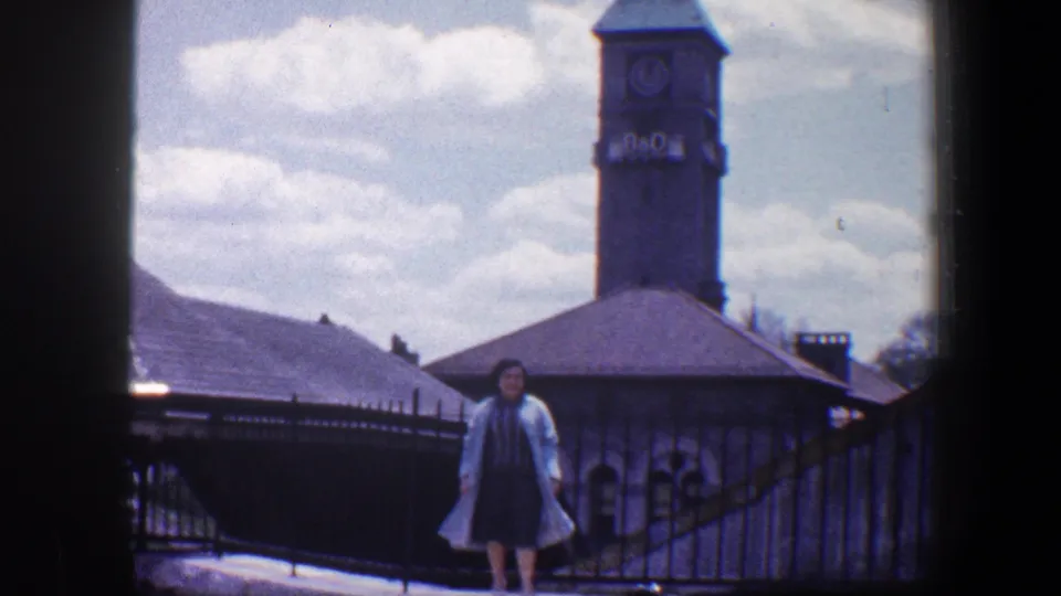 The woman stands on an outdoor walkway below the B&O clock tower, with railings, rooflines, and clouds visible.