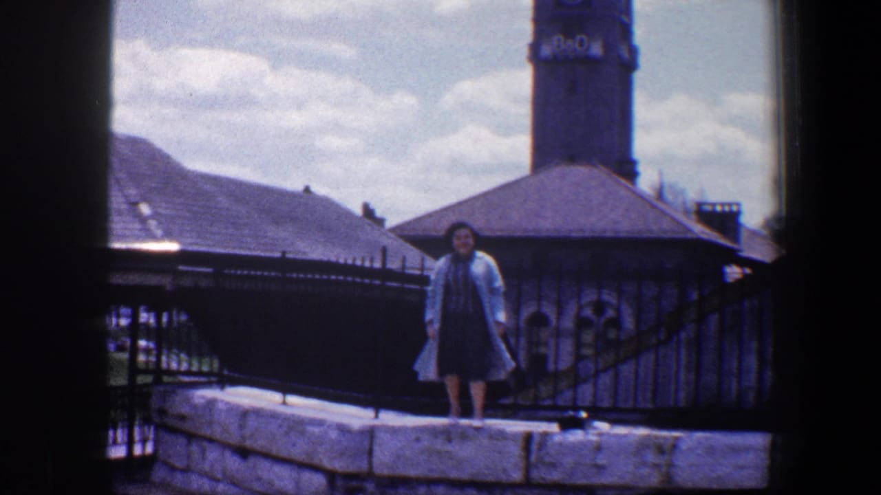 Woman standing on a stone wall near iron fencing and a tower.