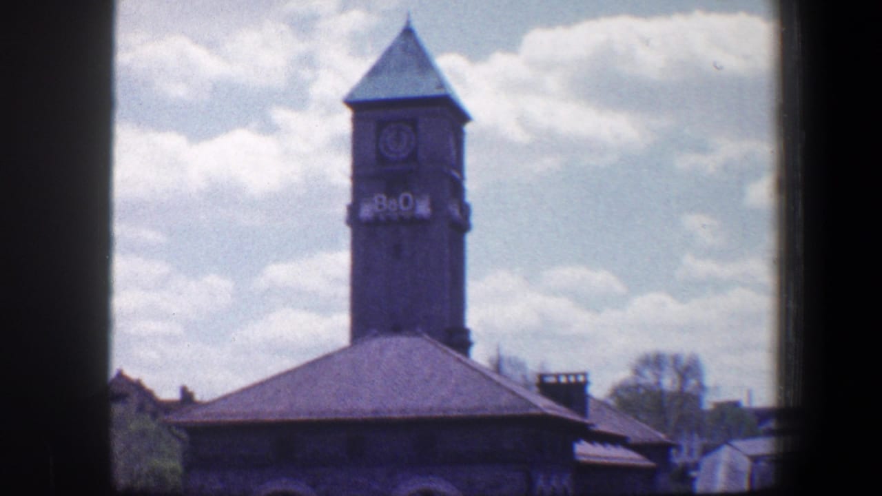 Clocktower and roof of a grey stone building seen through dark 8mm frame borders.