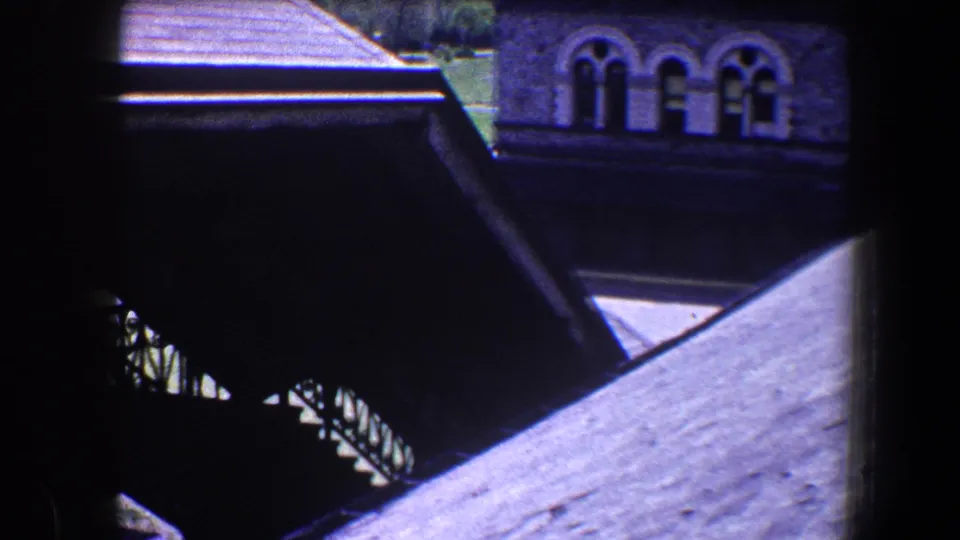 Elevated 1960 Baltimore view across a roof toward shaded exterior stairs and a stone facade with arched windows.