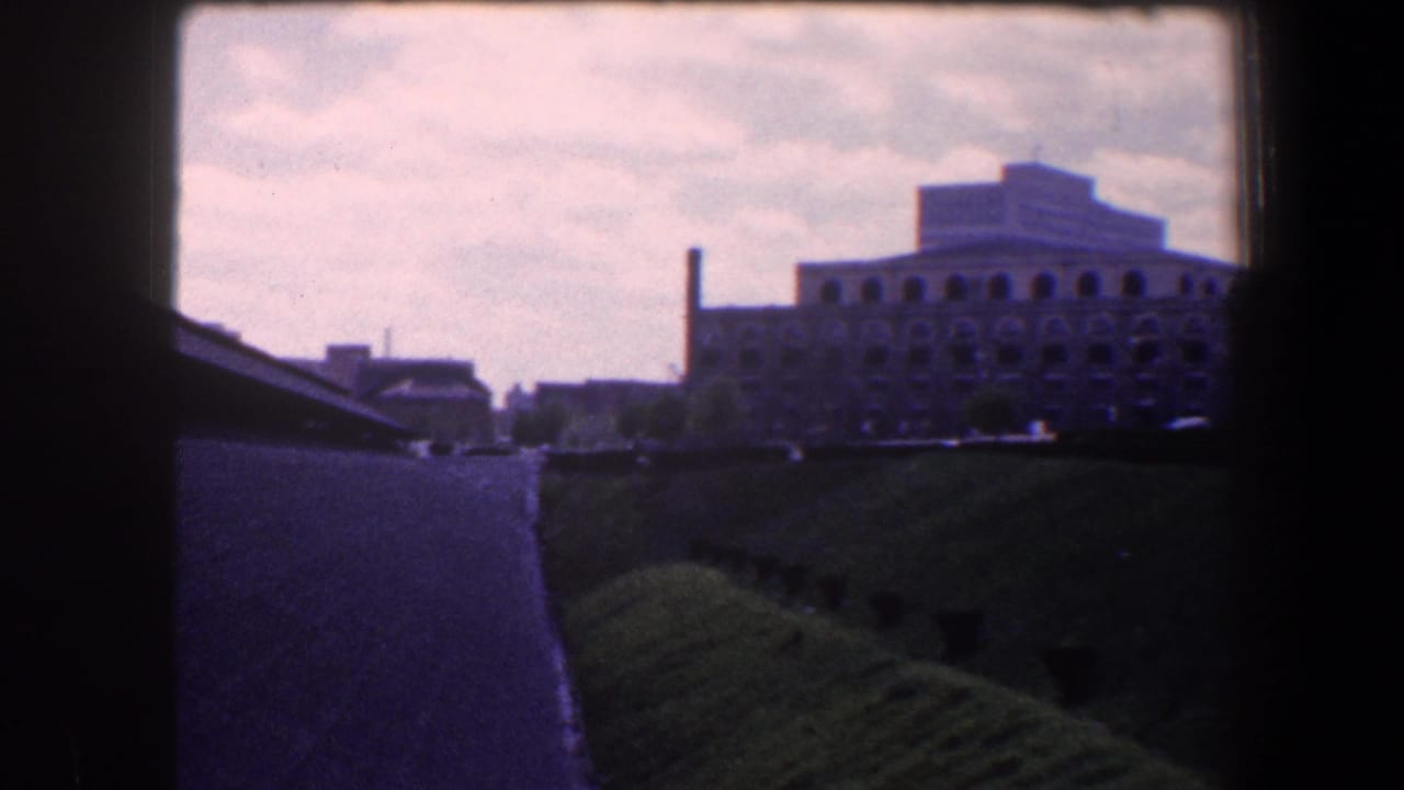 Large arched building and roadway viewed past a dark foreground frame.
