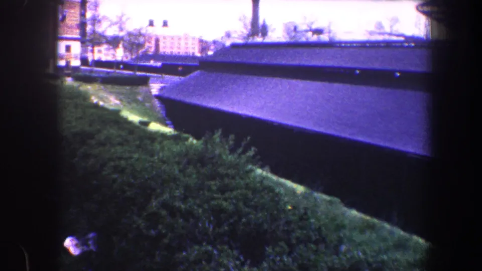 The view shifts to roadside grass, a dark linear structure, and distant Baltimore buildings under bright, faded sky.