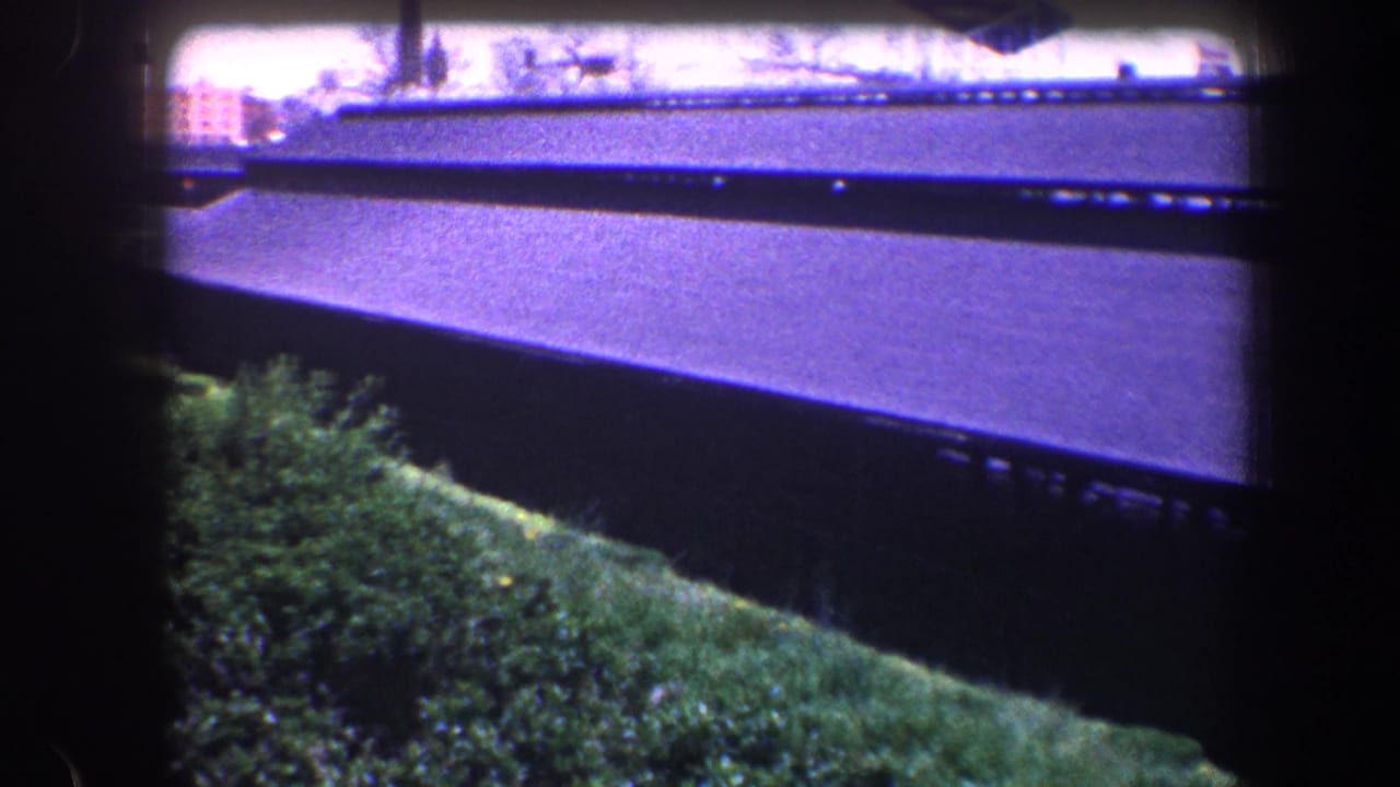 1960 Baltimore 8mm view of a dark roof edge above grass and shrubs, framed by heavy film borders.