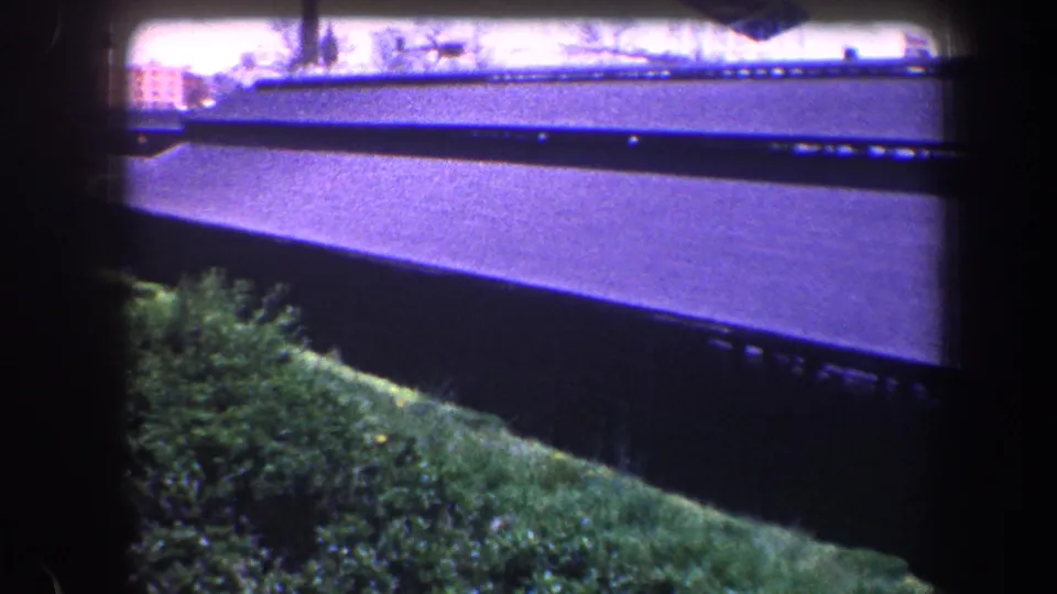 1960 Baltimore 8mm view of a dark roof edge above grass and shrubs, framed by heavy film borders.