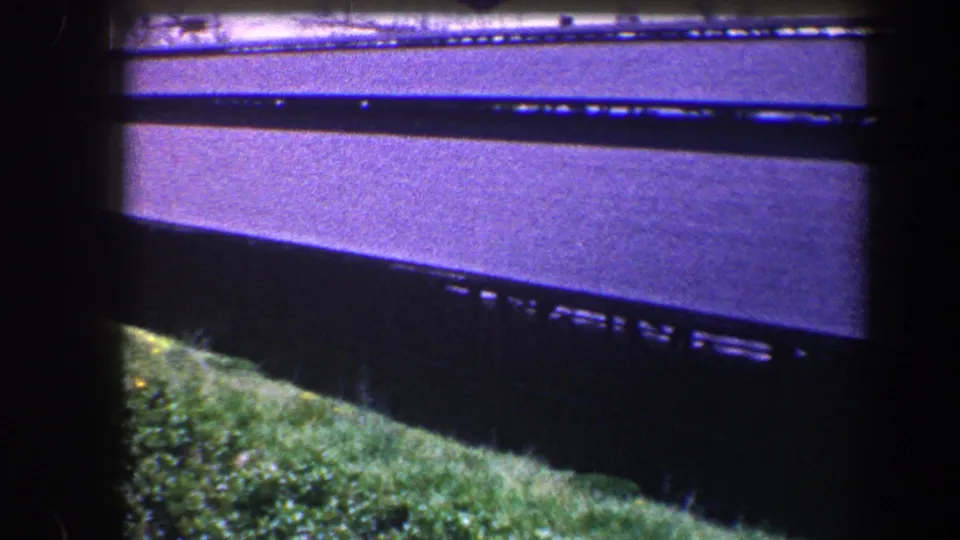 1960 Baltimore 8mm frame with a long dark roof crossing above grass, shrubs, and soft purple-tinted exposure.