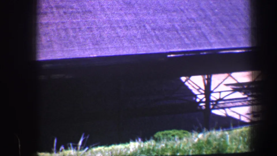 1960 Baltimore 8mm frame showing the roofed structure, metal supports, bright underside, and green grass in the foreground.