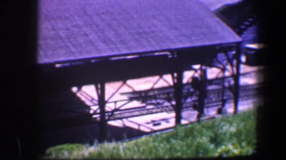 1960 Baltimore 8mm frame showing a roofed outdoor structure with metal braces, bright underside, and grass along the bottom edge.