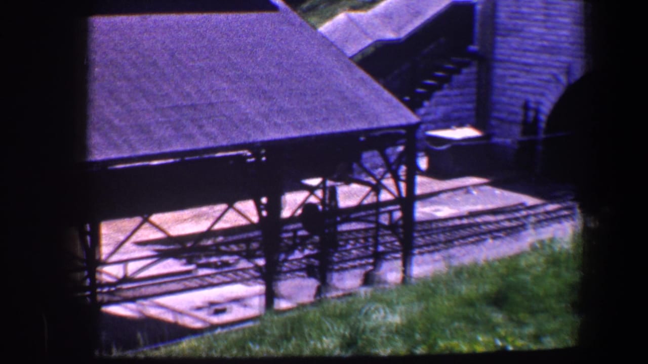 1960 Baltimore 8mm frame showing a model railway platform, tracks, stone bridge structure, and grass in a miniature layout.