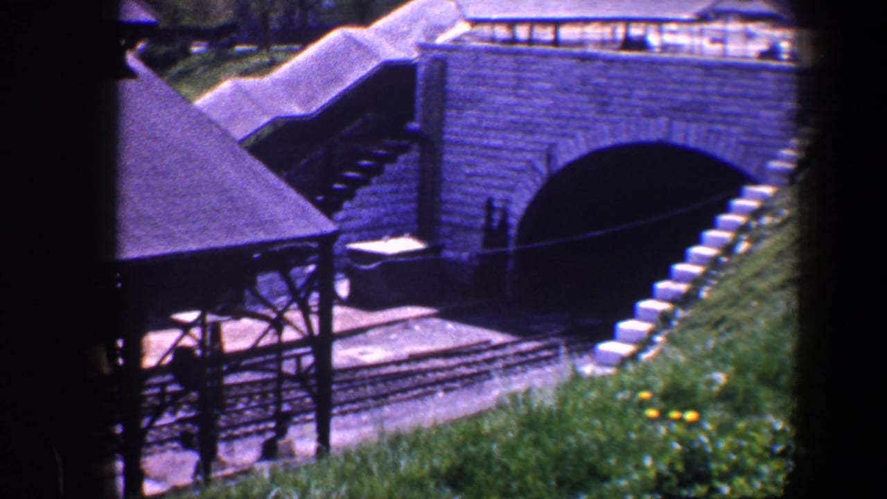 1960 Baltimore model railway scene with an arched tunnel portal, steps, covered platform, tracks, and sloped grass.