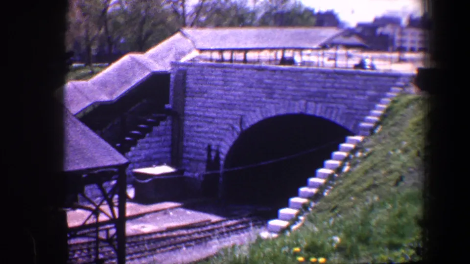 1960 Baltimore 8mm frame showing the model railway tunnel, stairway, tracks, grassy embankment, and distant structures.