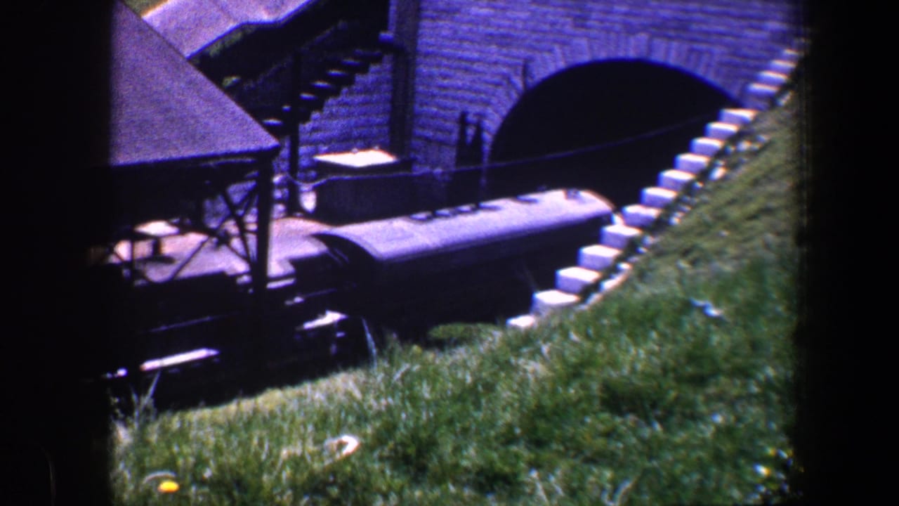 Train partly under the brick bridge beside a grassy slope.