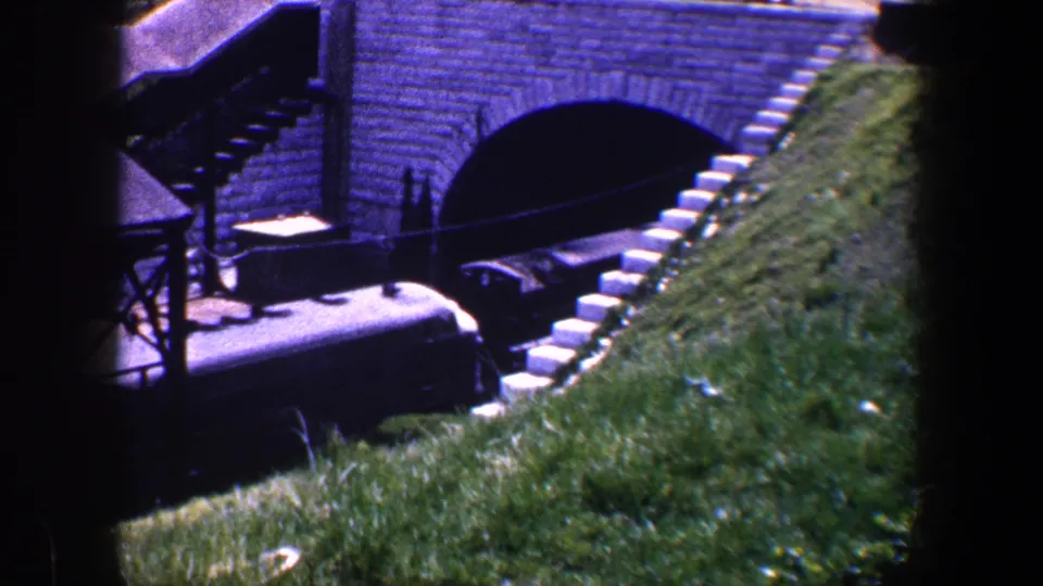 The final frame keeps the passing train, brick arch, and grassy embankment in view as the rail movement continues.