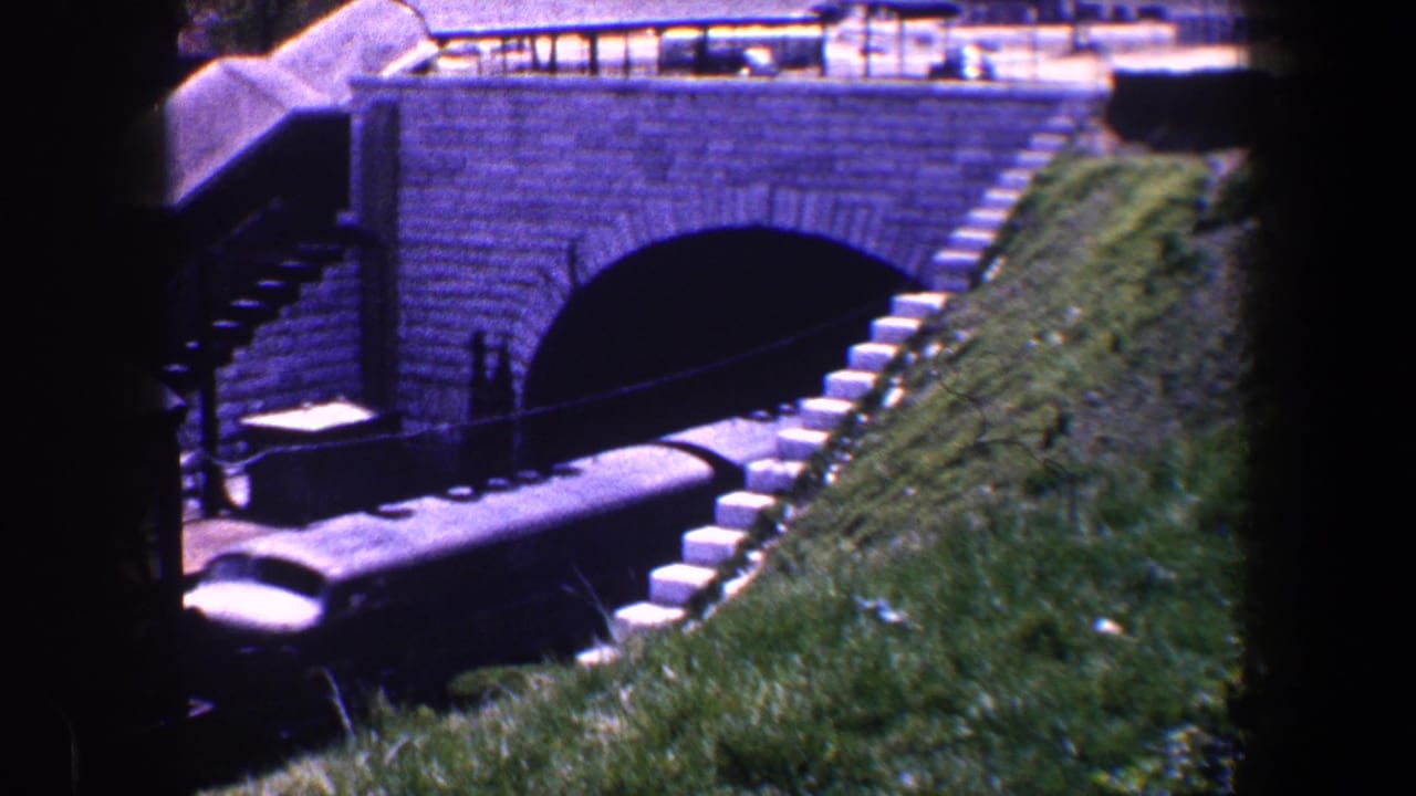 Baltimore rail scene from 1960 showing freight cars partly inside a dark arched tunnel with a sloped grassy bank beside the tracks.