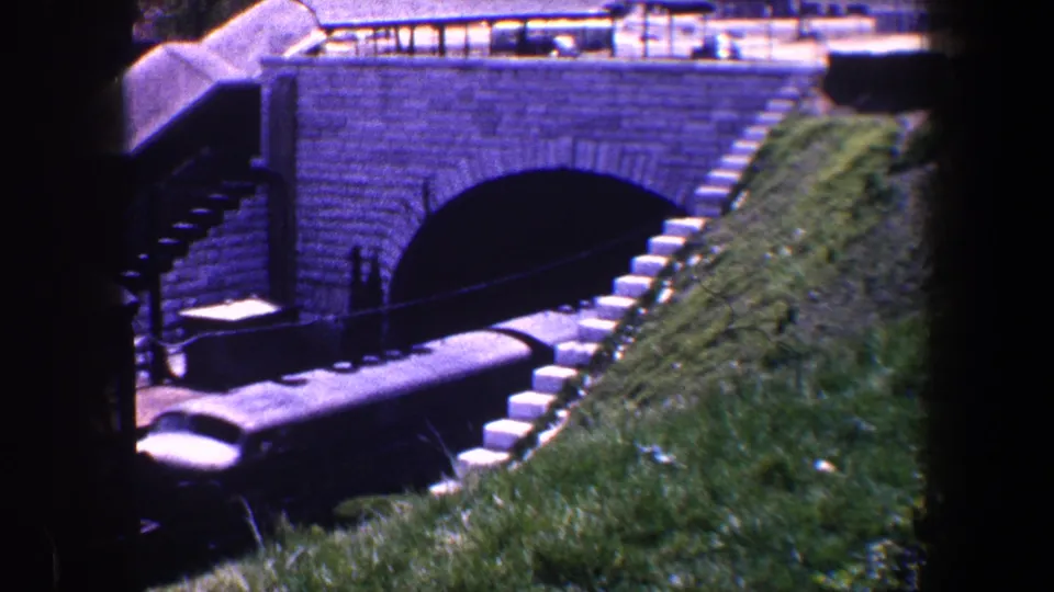Baltimore rail scene from 1960 showing freight cars partly inside a dark arched tunnel with a sloped grassy bank beside the tracks.
