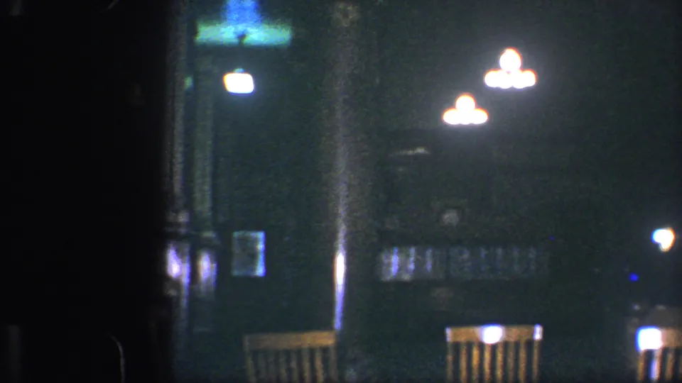 Baltimore 1960 home-movie frame of an empty restaurant area, with bright ceiling lights and chairs partly visible in darkness.