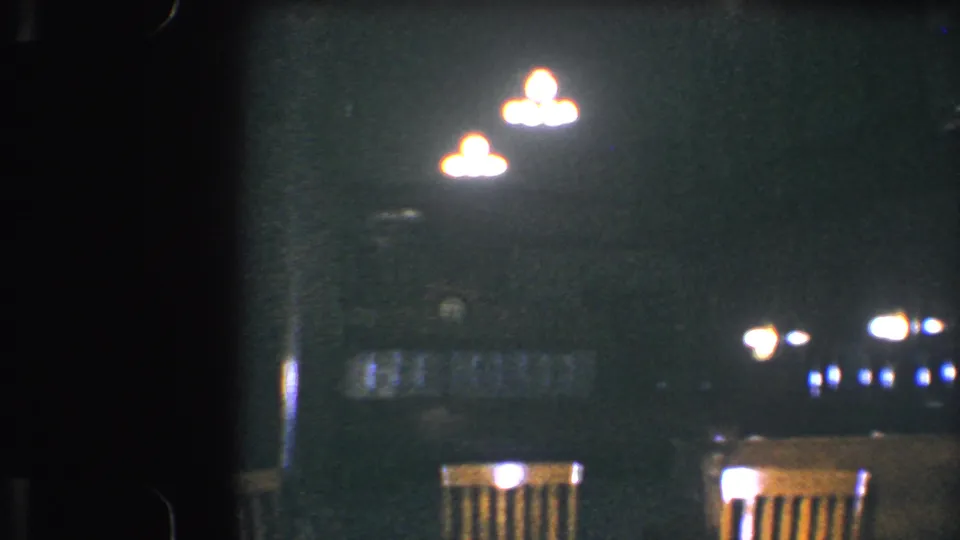 Baltimore 1960 frame of a quiet restaurant interior, where glowing lights illuminate chairs and tables in a dark room.