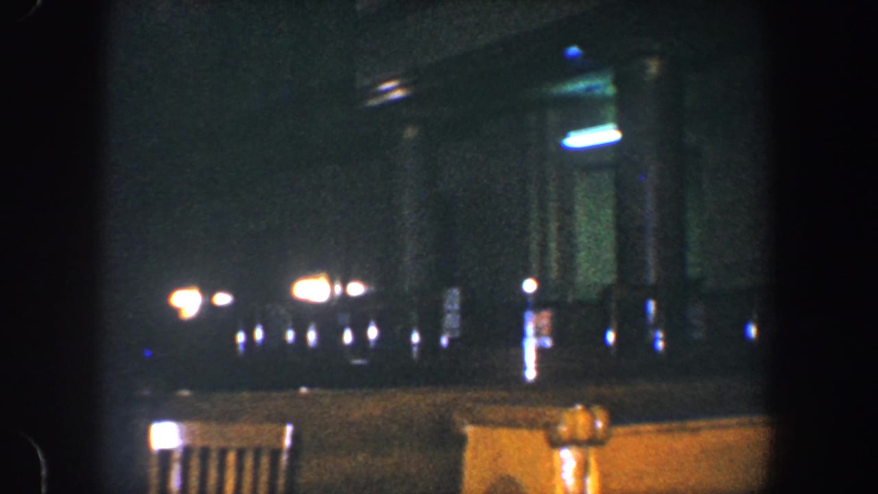 Dark interior with faint lights, vertical supports, and partial chair backs in the foreground.