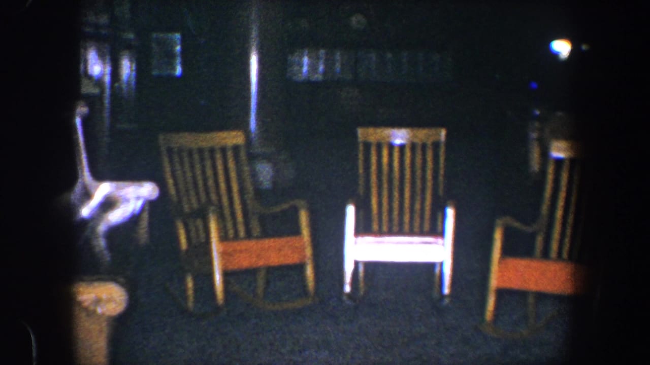 1960 Baltimore 8mm frame showing three wooden rocking chairs in a dim interior with a bright partial object at the left edge.