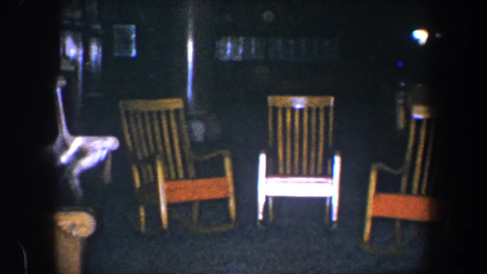 1960 Baltimore 8mm frame showing three wooden rocking chairs in a dim interior with a bright partial object at the left edge.