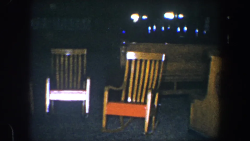 1960 Baltimore 8mm frame with two wooden rocking chairs in a dark interior and bright reflections near the top of the frame.