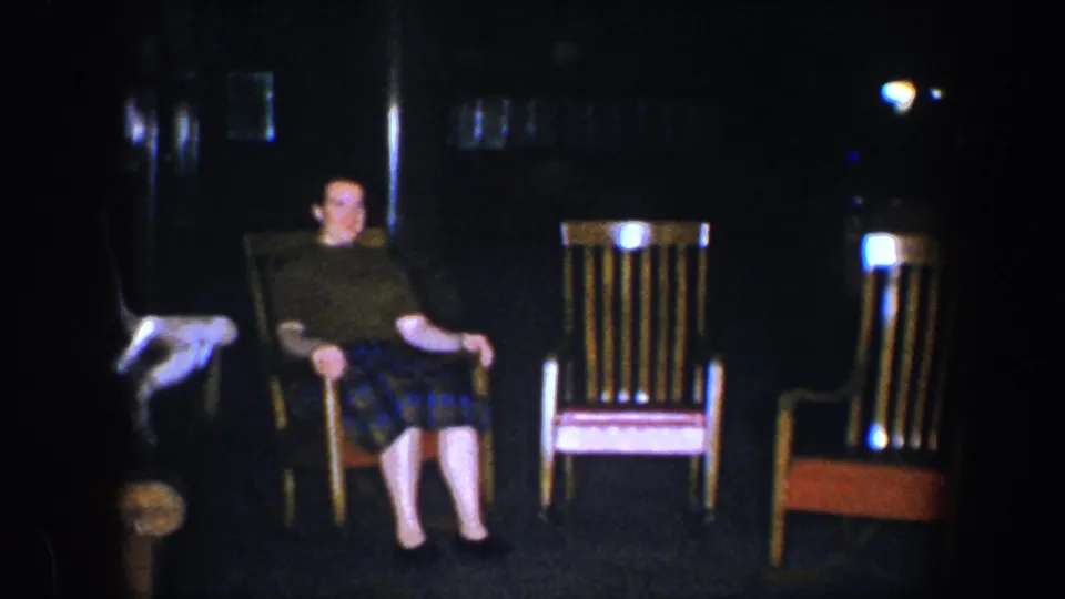 Near the end of the clip, the woman is still seated in the rocking chair, framed by other wooden chairs in the Baltimore home interior.
